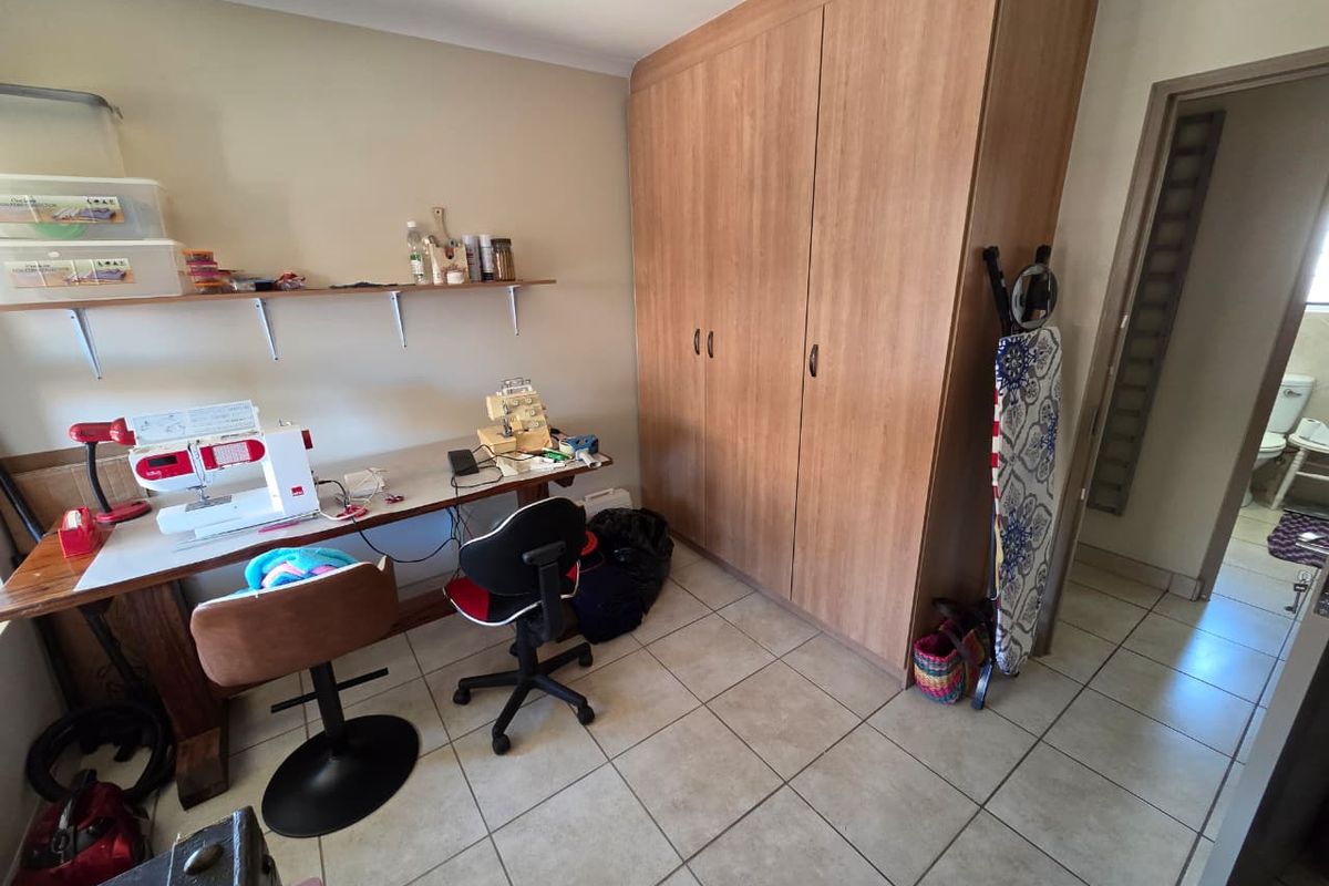 A functional bedroom featuring tiled flooring, a large built-in wooden wardrobe, and wall-mounted shelving, currently utilized as a workspace.