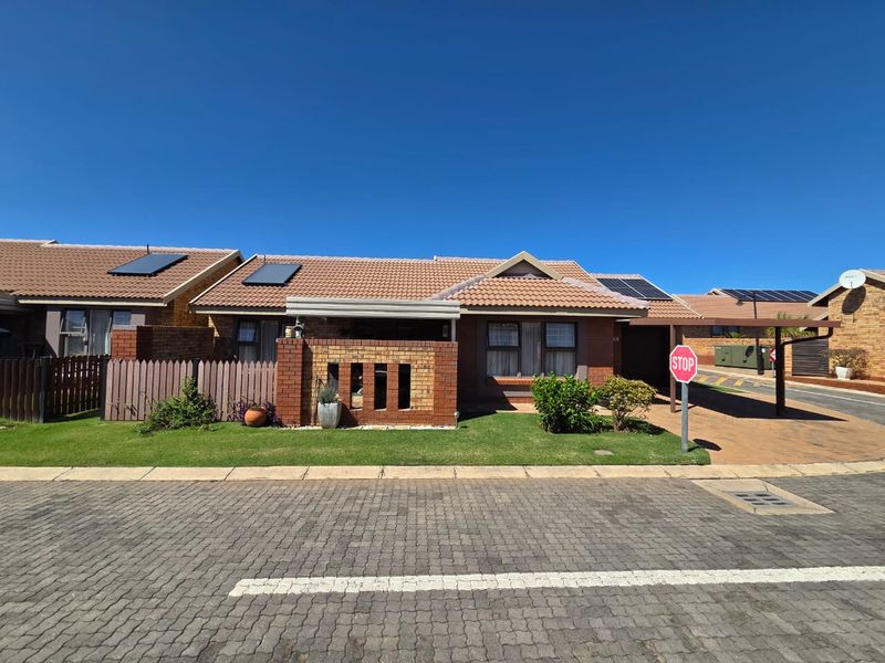 Front elevation of a single-story townhouse featuring a tiled roof, solar panels, brick facade, and a paved driveway with a carport.