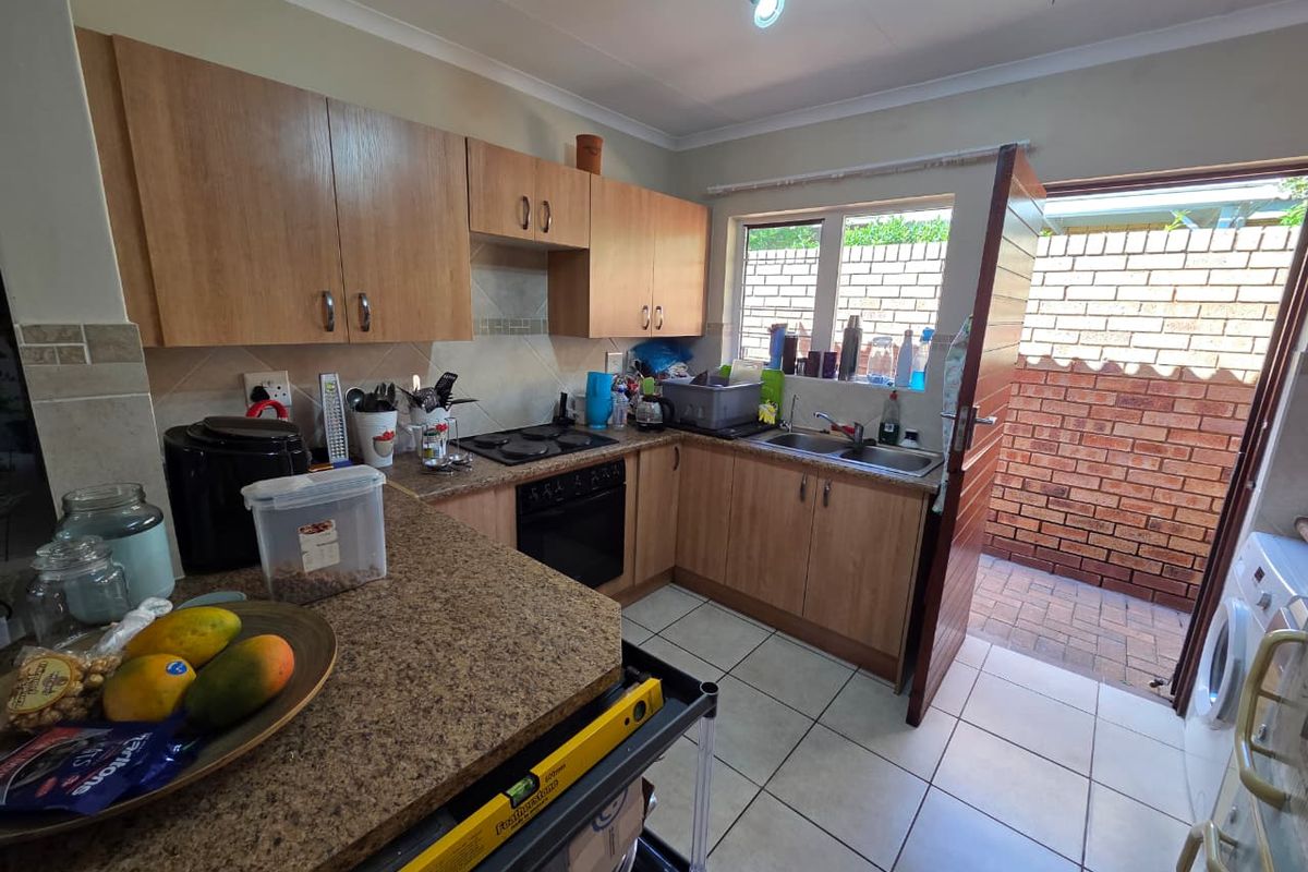 Functional kitchen featuring light wood cabinetry, laminate countertops, built-in oven and hob, and direct access to an exterior paved courtyard area.
