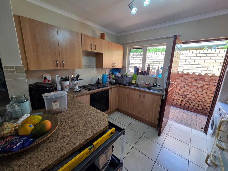 Functional kitchen featuring light wood cabinetry, laminate countertops, built-in oven and hob, and direct access to an exterior paved courtyard area.