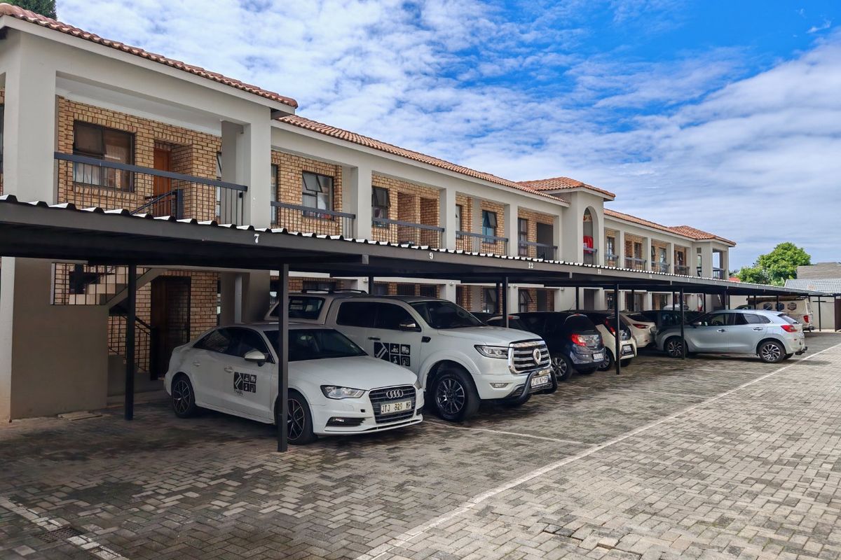 Exterior view of a commercial property featuring a multi-level building with covered parking bays and paved driveway access.
