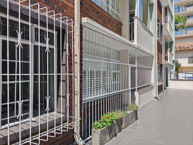 Exterior view of an apartment building facade featuring brickwork, security bars on windows, and a concrete walkway.