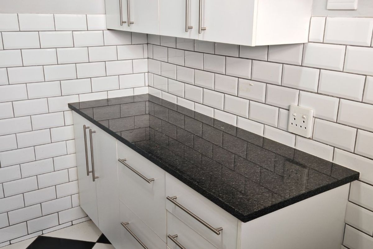 A clean, modern kitchen area featuring white cabinetry, black granite countertops, and a classic white subway tile backsplash.