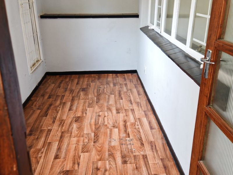A bright, empty enclosed balcony or sunroom featuring wood-look laminate flooring, timber-framed glass doors, and tiled window sills.
