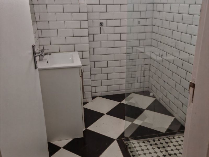 A clean, modern bathroom featuring a vanity basin, glass shower enclosure, classic subway wall tiling, and distinctive black and white checkered floor tiles.