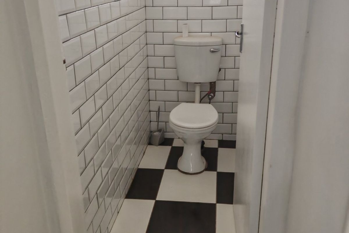 A compact bathroom featuring white subway wall tiles, a black and white checkered floor, and a functional toilet.