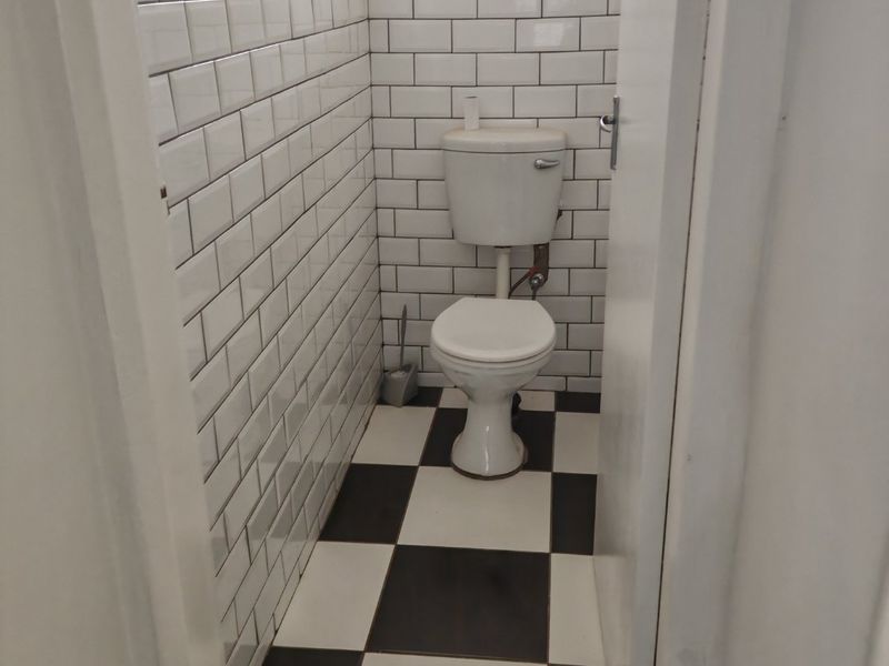 A compact bathroom featuring white subway wall tiles, a black and white checkered floor, and a functional toilet.