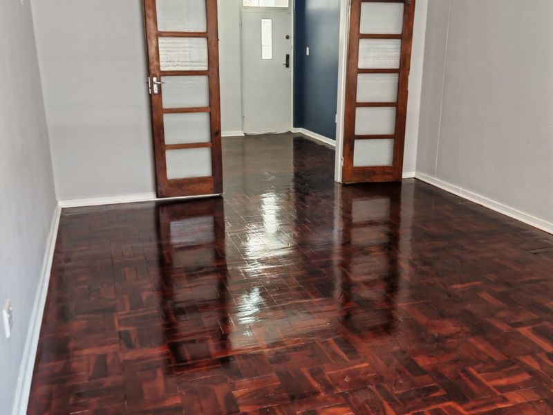 An empty living room featuring polished parquet flooring and classic double wooden doors leading to an entrance area.