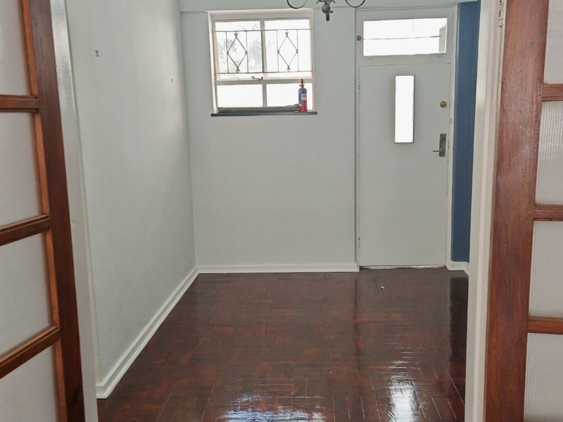An empty entrance hall featuring polished parquet flooring, a security door, and timber-framed glass doors leading into the space.