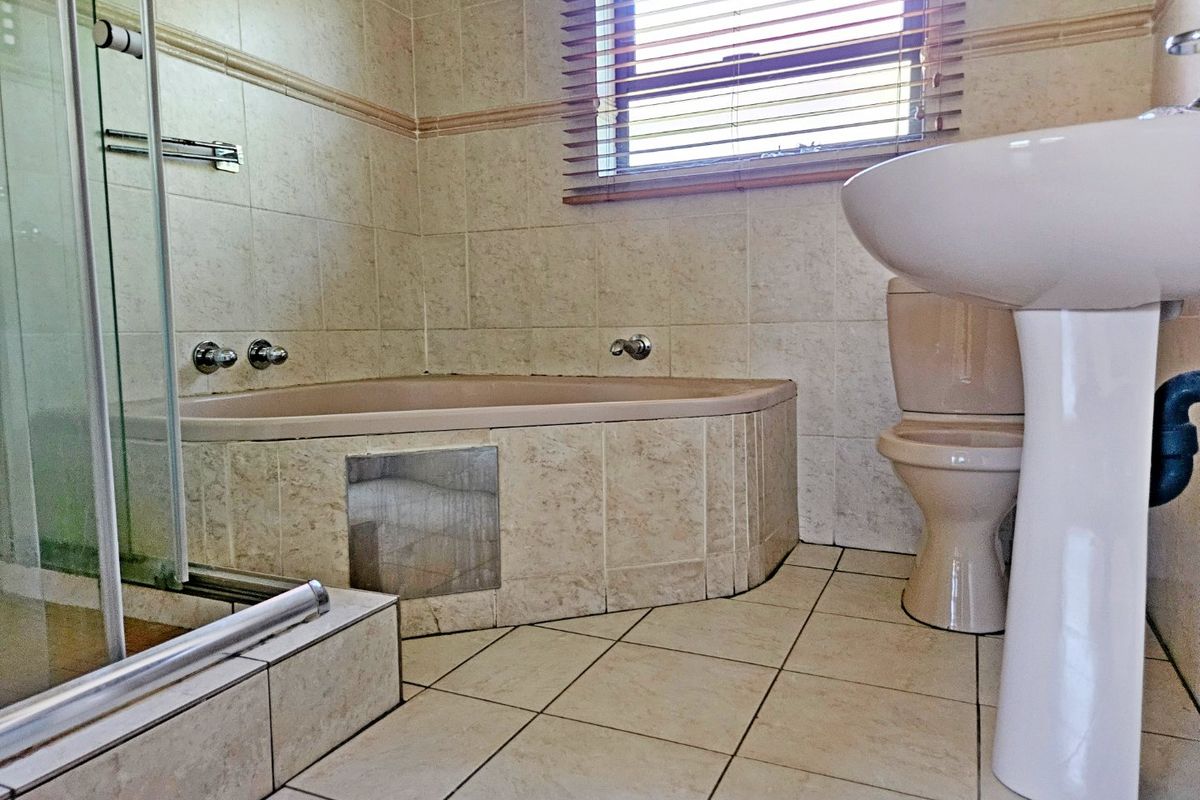 A functional bathroom featuring a built-in bathtub, separate shower enclosure, pedestal basin, and toilet with neutral tiled finishes.