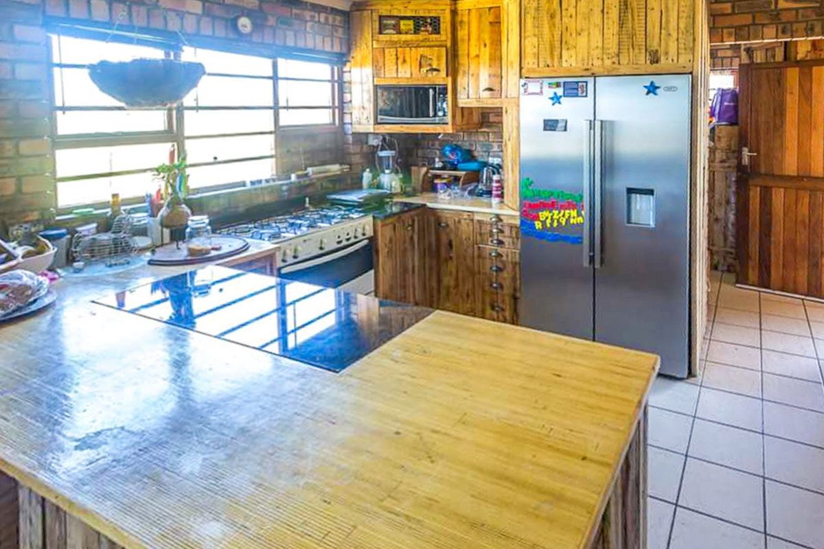 Rustic kitchen featuring exposed brick walls, wooden cabinetry, a gas stove, and a large wooden island countertop with tiled flooring.