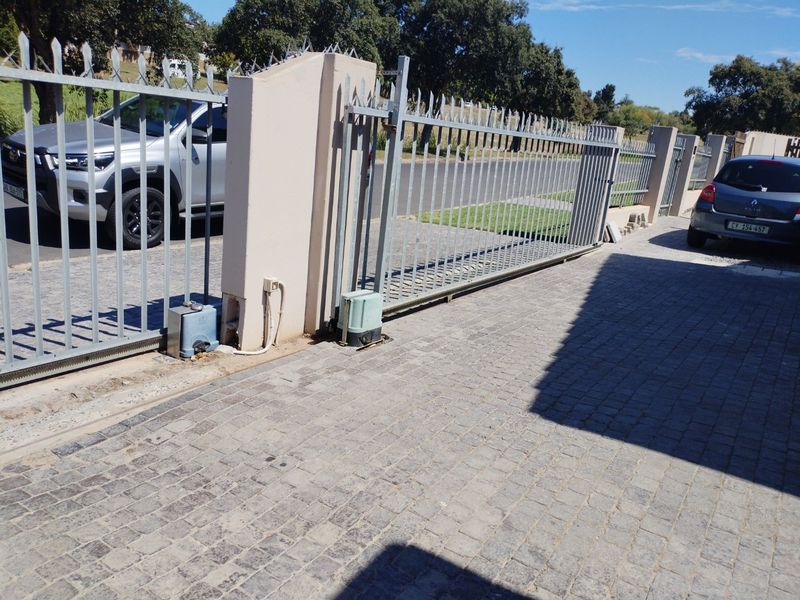 Front entrance area featuring a sliding security gate with an automated motor and paved driveway surface.
