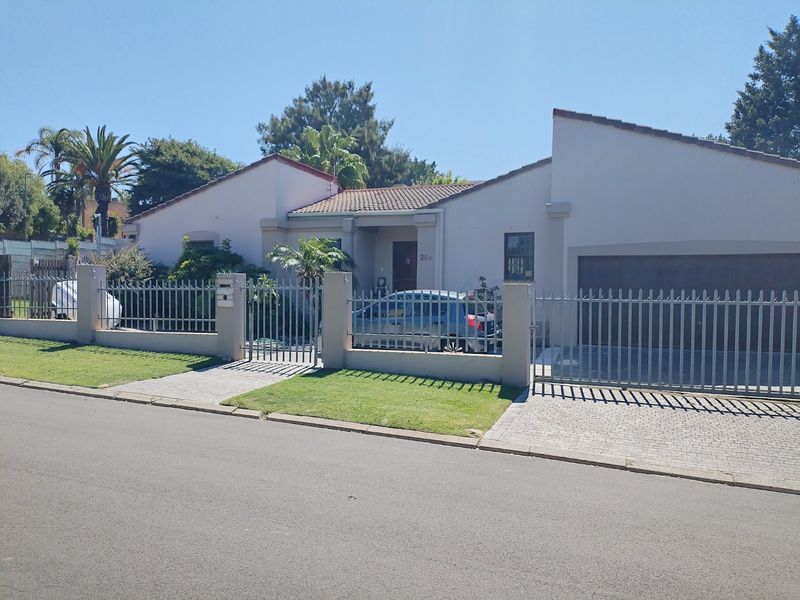 Front elevation of a single-story house featuring a paved driveway, metal perimeter fencing, and a secure garage entrance.