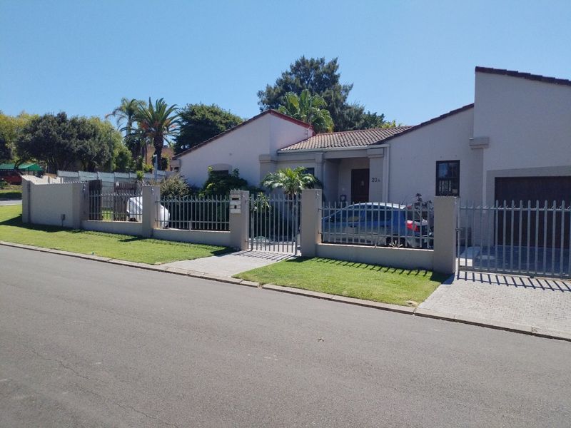 Front view of a single-story residential house featuring a tiled roof, paved driveway, and secure metal perimeter fencing.