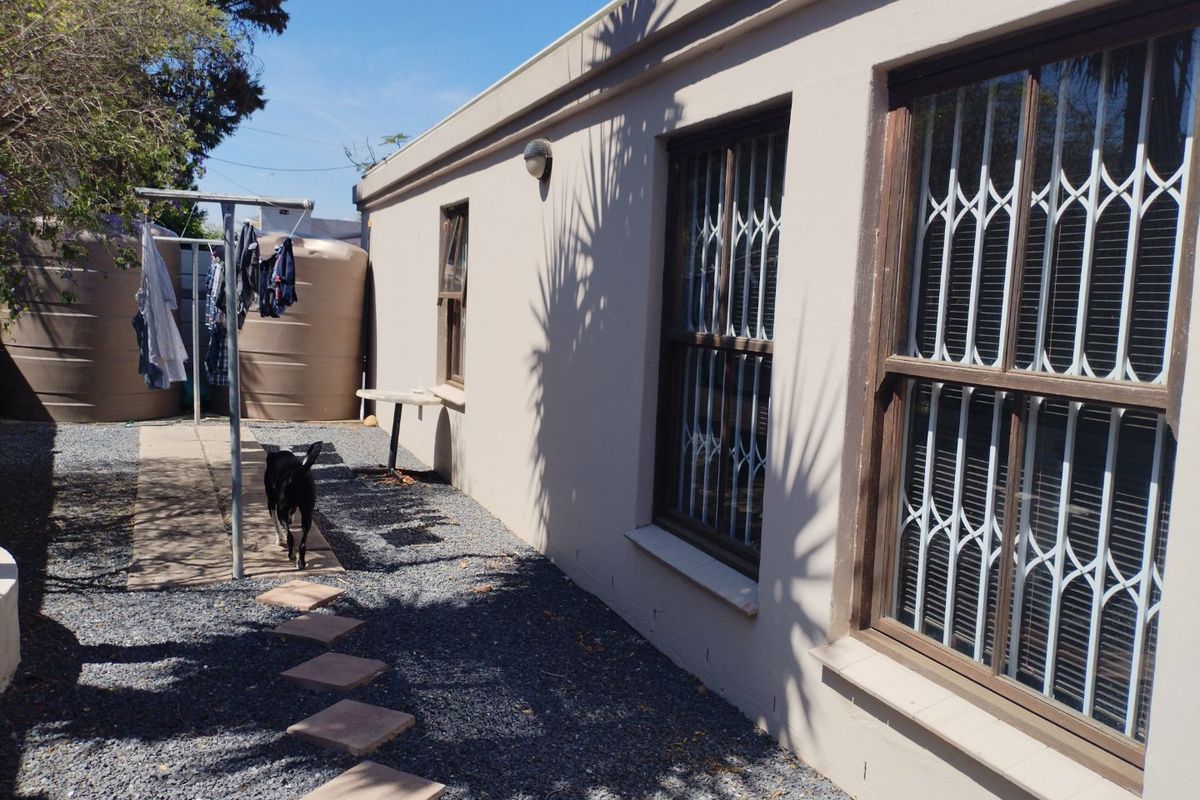 Rear exterior view of the property featuring gravel landscaping, water storage tanks, and windows fitted with security bars.