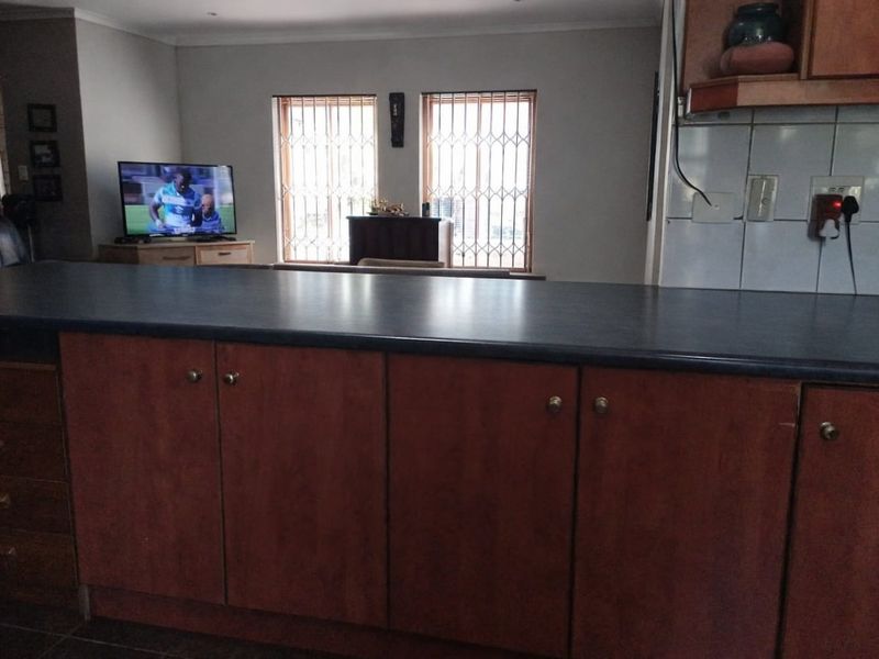 Open plan kitchen area featuring a central island with laminate cabinetry and countertop, overlooking a living space with security-barred windows.