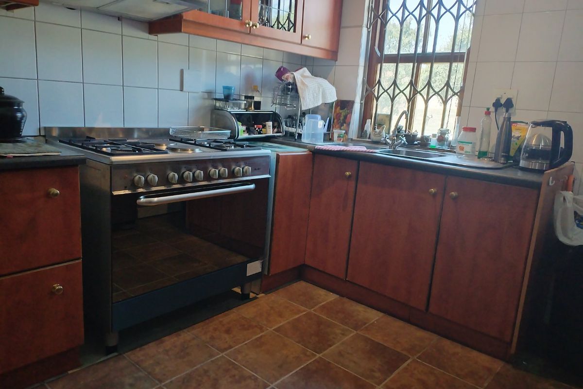 A functional kitchen featuring wooden cabinetry, a gas stove with extractor fan, tiled backsplash, and a double sink with a security-gated window.