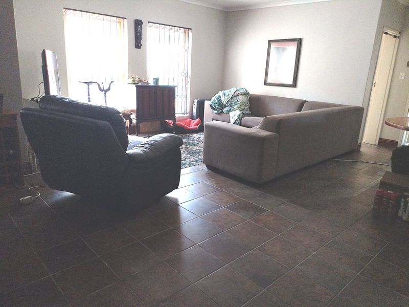 A living room featuring dark ceramic floor tiles, large windows with vertical blinds, and security bars.