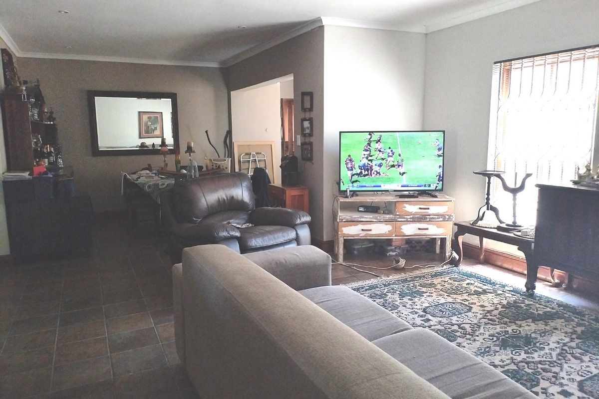 A spacious living room featuring tiled flooring, recessed downlighting, and a large window with security bars, offering a comfortable and functional living space.