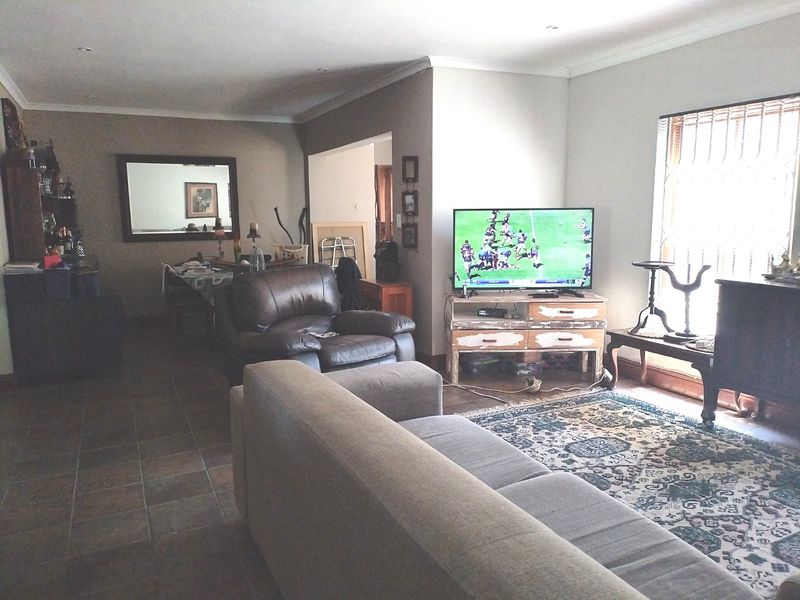A spacious living room featuring tiled flooring, recessed downlighting, and a large window with security bars, offering a comfortable and functional living space.