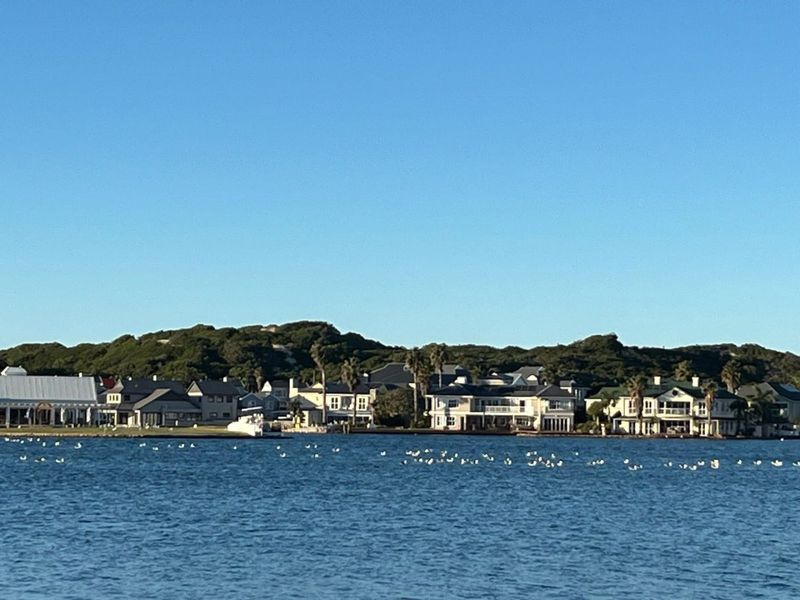 A scenic water-level view of a coastal residential estate featuring multiple luxury homes situated along the shoreline.