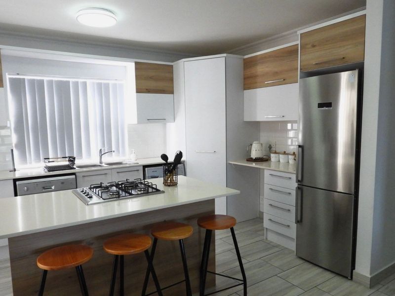 Modern kitchen featuring a central island with a gas hob, stone countertops, ample built-in cabinetry, and high-quality tiled flooring.