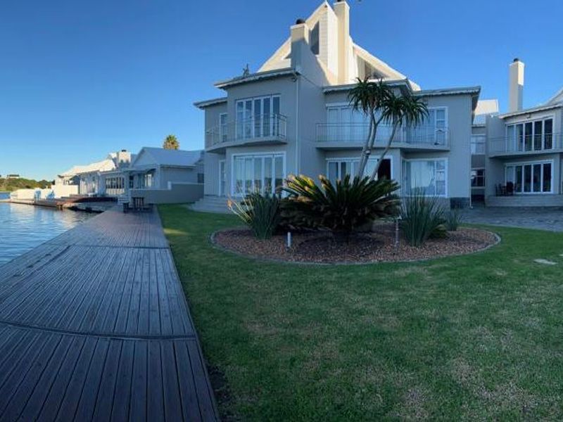 Rear view of a multi-story apartment building featuring timber decking, balconies, and direct waterfront access with landscaped garden areas.