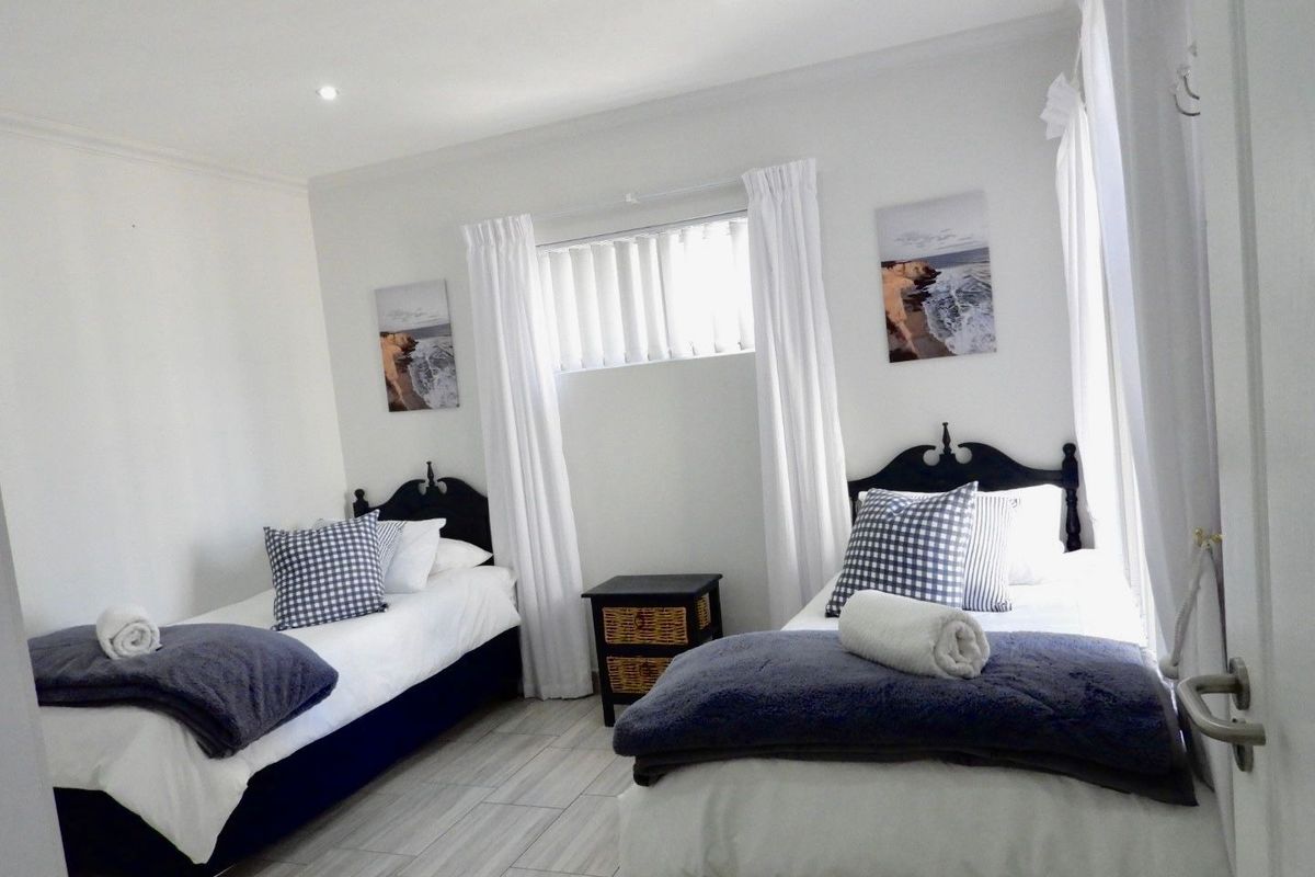 A bright and well-maintained bedroom featuring neutral tiled flooring, recessed downlighting, and functional window treatments.