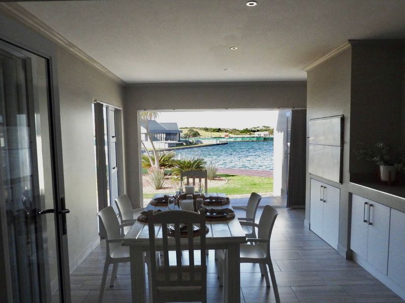 An open-plan dining area featuring tiled floors, recessed lighting, and large sliding doors that open to a scenic waterfront view.