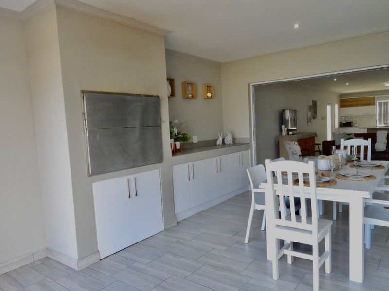 Open-plan dining area featuring tiled flooring, built-in cabinetry, and a stainless steel built-in braai, with a seamless transition to the adjacent living space.