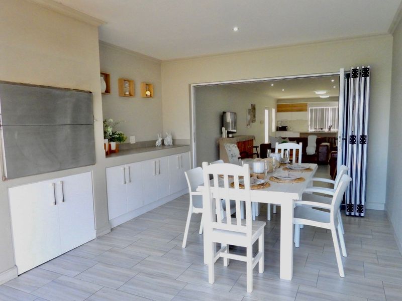 Open-plan dining area featuring built-in cabinetry, a stone countertop, and a built-in braai, with bi-fold doors connecting to the main living space.