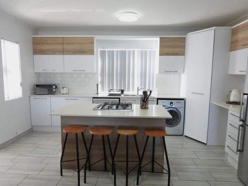 Modern kitchen featuring two-tone cabinetry, stone countertops, a central island with a gas hob, and integrated laundry facilities.