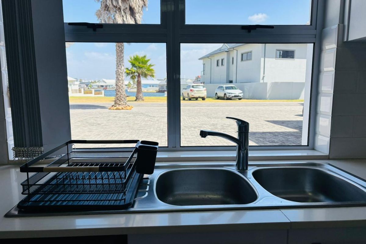 A clean kitchen sink area featuring a double bowl stainless steel basin, chrome mixer tap, and subway tile backsplash with a view of the exterior.