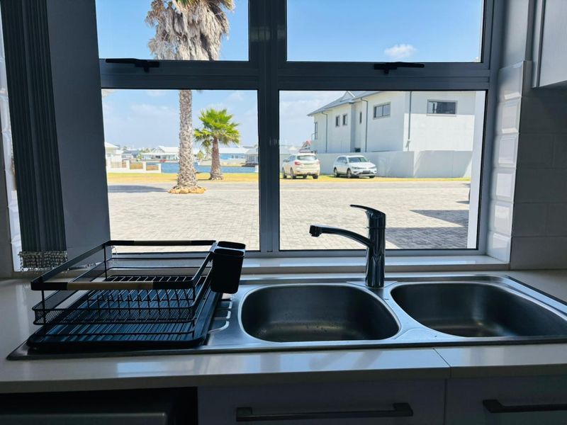 A clean kitchen sink area featuring a double bowl stainless steel basin, chrome mixer tap, and subway tile backsplash with a view of the exterior.