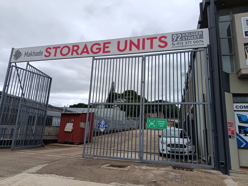 Front entrance to commercial storage facility featuring a large metal security gate, paved driveway access, and prominent business signage.