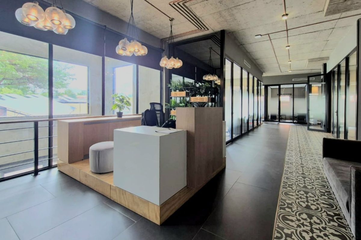 Modern commercial office space featuring an exposed concrete ceiling, glass partitions, built-in reception desk, and a mix of large format and decorative patterned floor tiles.