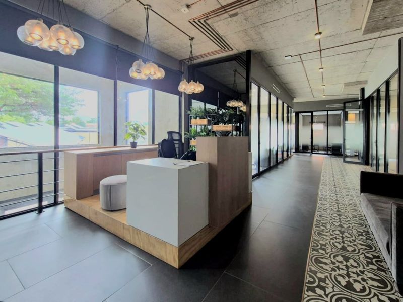 Modern commercial office space featuring an exposed concrete ceiling, glass partitions, built-in reception desk, and a mix of large format and decorative patterned floor tiles.