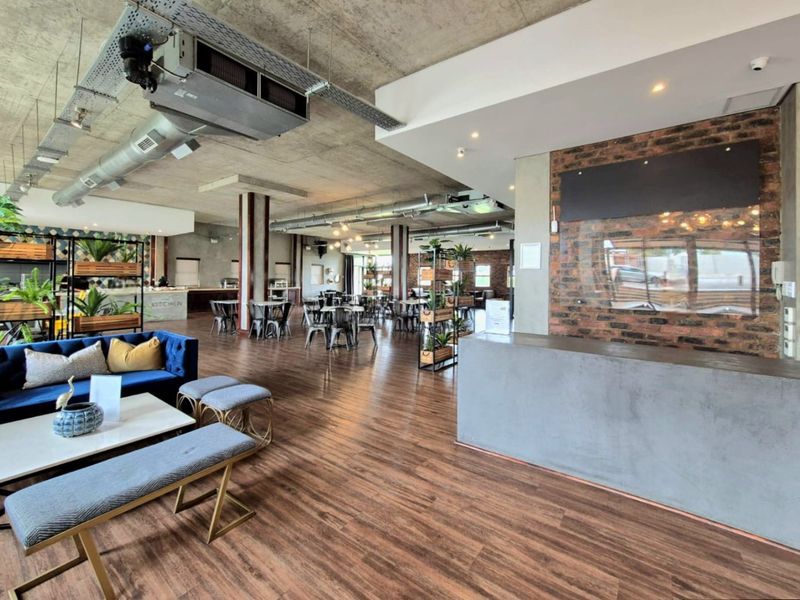 Spacious open-plan commercial area featuring industrial-style exposed concrete ceilings, HVAC ducting, exposed brickwork, and a modern concrete reception desk.
