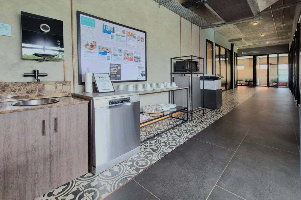 A modern commercial kitchenette featuring stone countertops, built-in cabinetry, and industrial-style exposed ceiling ducting with a mix of patterned and large format floor tiles.