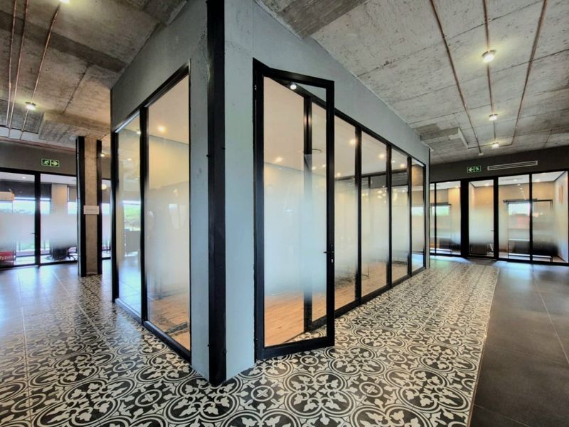 Modern commercial office space featuring industrial-style exposed concrete ceilings, glass-partitioned meeting rooms, and decorative patterned floor tiles.