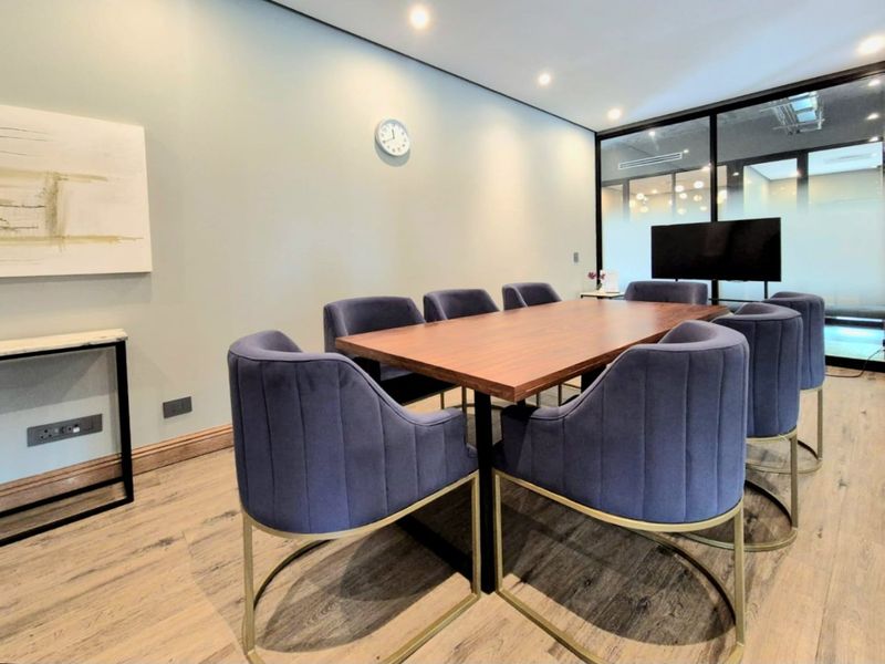 A modern, well-maintained office meeting room featuring wood-look flooring, recessed lighting, and a contemporary glass partition wall.