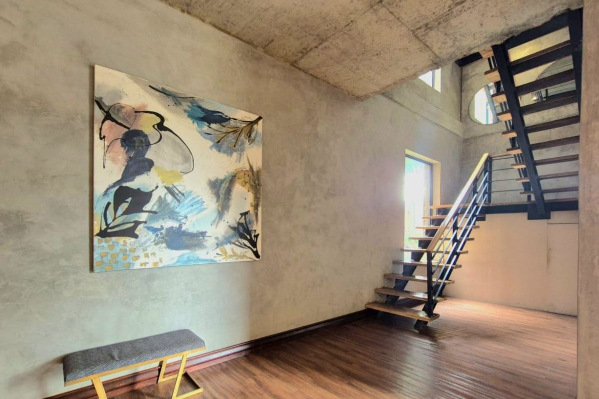 Modern industrial-style entrance hall featuring exposed concrete ceilings, timber flooring, and a striking open-tread metal staircase.