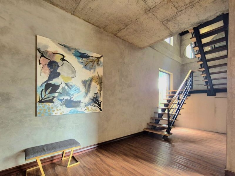 Modern industrial-style entrance hall featuring exposed concrete ceilings, timber flooring, and a striking open-tread metal staircase.