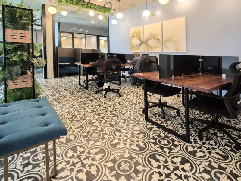 Modern open-plan office space featuring exposed concrete ceilings, decorative patterned floor tiles, and glass-partitioned meeting areas.