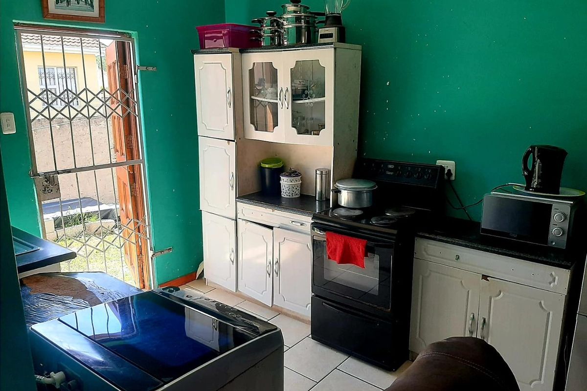 A functional kitchen area featuring built-in cabinetry, an electric stove, and tiled flooring, with direct access to the exterior via a security gate.