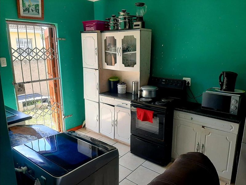 A functional kitchen area featuring built-in cabinetry, an electric stove, and tiled flooring, with direct access to the exterior via a security gate.