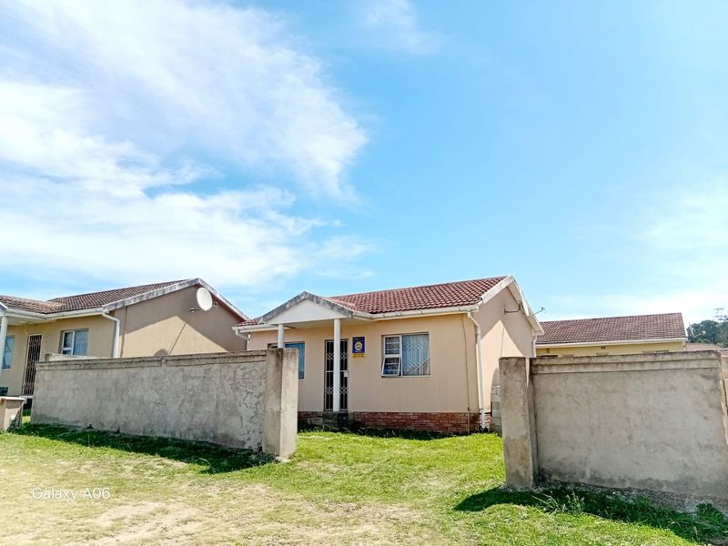Front view of a single-story residential house featuring a tiled roof, security gate, and a surrounding concrete perimeter wall.