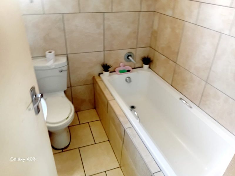 A functional bathroom featuring a built-in bathtub, toilet, and neutral ceramic tiling throughout the walls and floor.