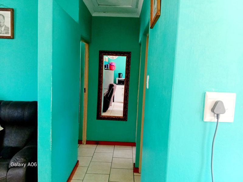 A narrow interior hallway featuring tiled flooring and bright teal painted walls, providing access to adjacent rooms.