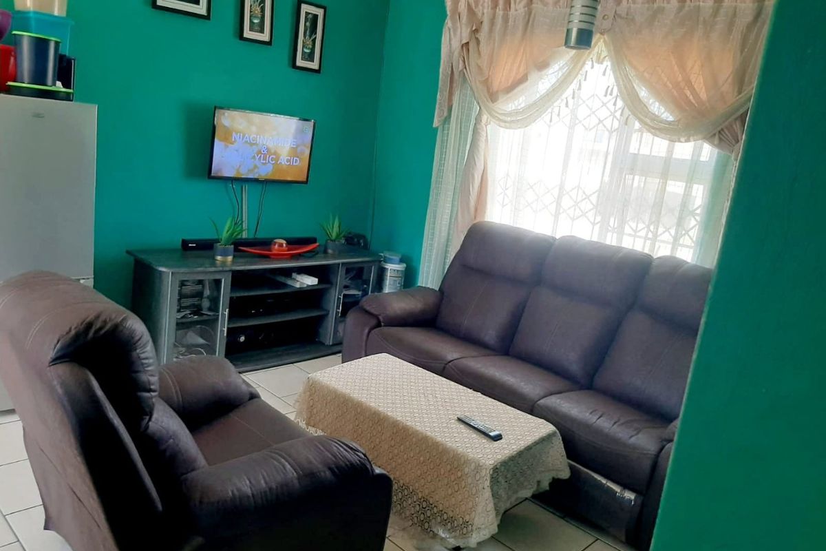 A living room featuring tiled flooring and a window fitted with security bars and curtain rails.